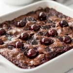 Warm chocolate cherry dump cake in a white baking dish with a spoonful served beside it