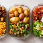 Loaded potato taco bowl meal prep with roasted potatoes, taco meat, cheese, beans, lettuce, tomatoes, and Greek yogurt on a white kitchen counter.