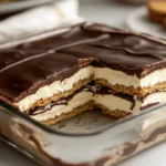 A sliced no-bake chocolate eclair dessert in a glass dish with creamy vanilla layers and glossy chocolate topping
