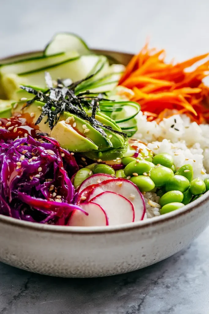 Rainbow Vegan Sushi Bowls 2 Close-up of a vegan sushi bowl with colorful vegetables, avocado, rice, nori, and sesame drizzle.