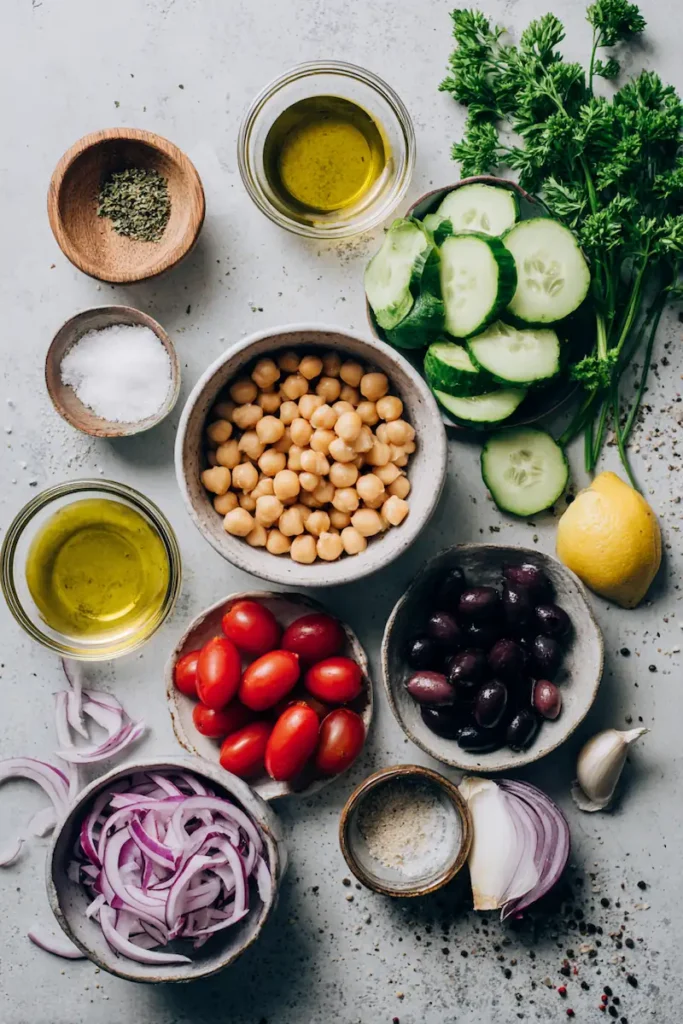 Mediterranean Chickpea Salad Bowls 3 Ingredients for Mediterranean chickpea salad bowls including chickpeas, cucumber, tomatoes, olives, parsley, tahini, and lemon