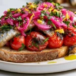 Rustic sourdough toast topped with sardines, roasted cherry tomatoes, pickled red onions, and parsley.