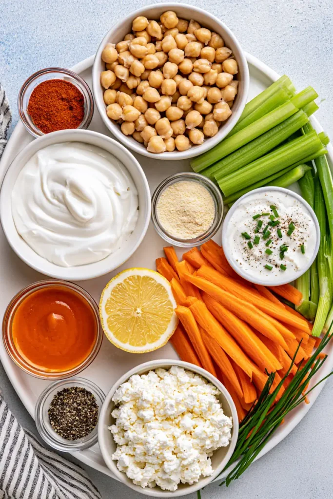 High-Protein Buffalo Chickpea Salad 2 Chickpeas, Greek yogurt, cottage cheese, Buffalo sauce, celery, carrots, and green onions arranged on a counter