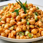 Creamy high-protein Buffalo chickpea salad served in a white bowl with celery and green onions