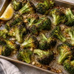 Roasted broccoli florets with browned edges on a metal sheet pan, served with lemon.